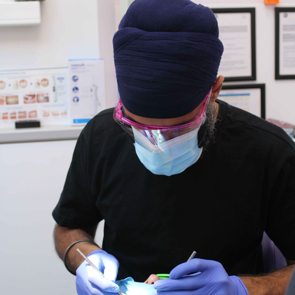 Dentist wearing a blue turban, mask and gloves treating a patient's teeth in a dental surgery